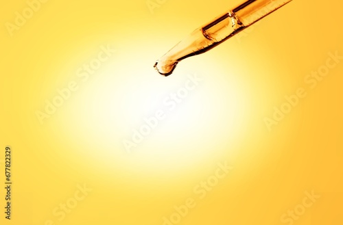 Glass lab dropper with yellow liquid on background, skincare serum