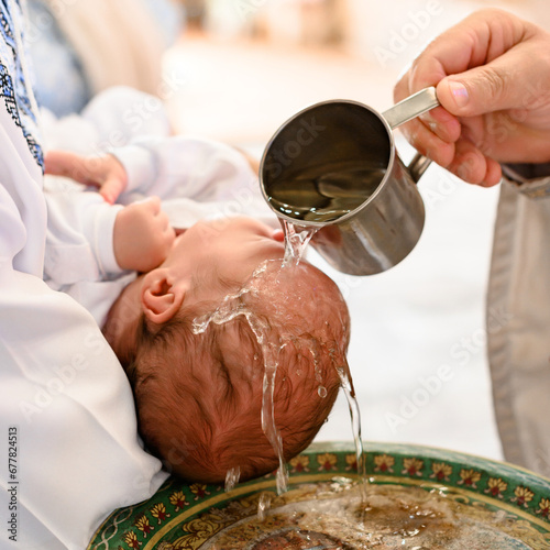 A priest pours water on the head of a small child during a Christian rite of baptism in a church.