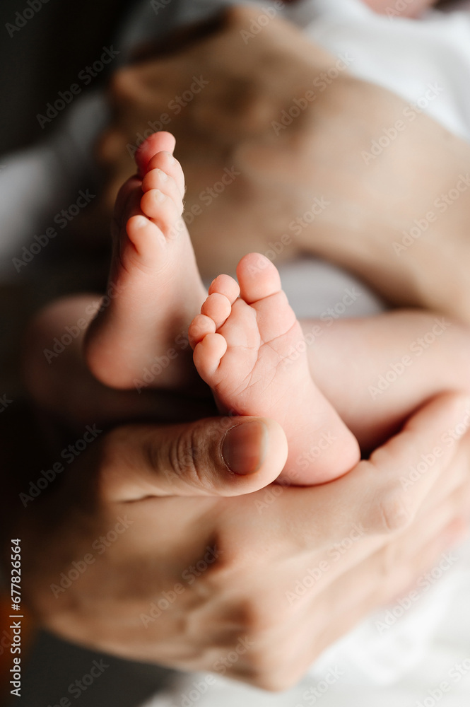 A mother holds the small legs of her newborn baby in her hands.