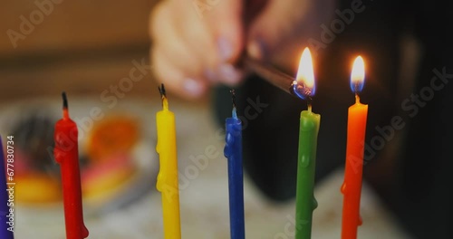 A woman's hand lights colored Hanukkah candles on the holiday. Medium shot horizontal panorama photo