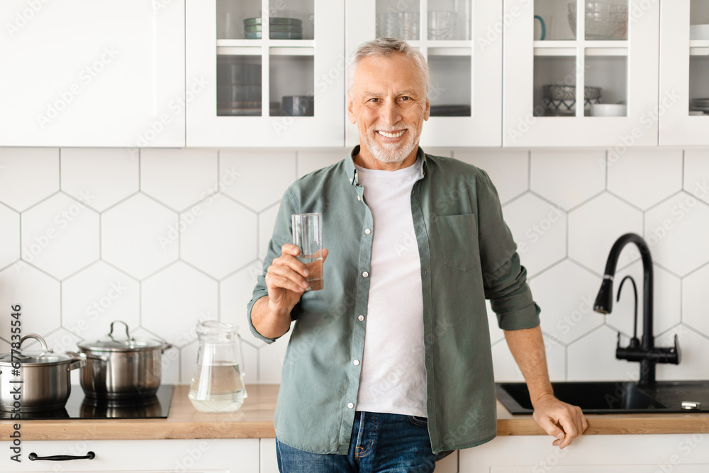 Smiling Senior Man With Glass Of Water In Hand Posing In Kitchen Smiling Senior Man With Glass Of Water In Hand Posing In Kitchen