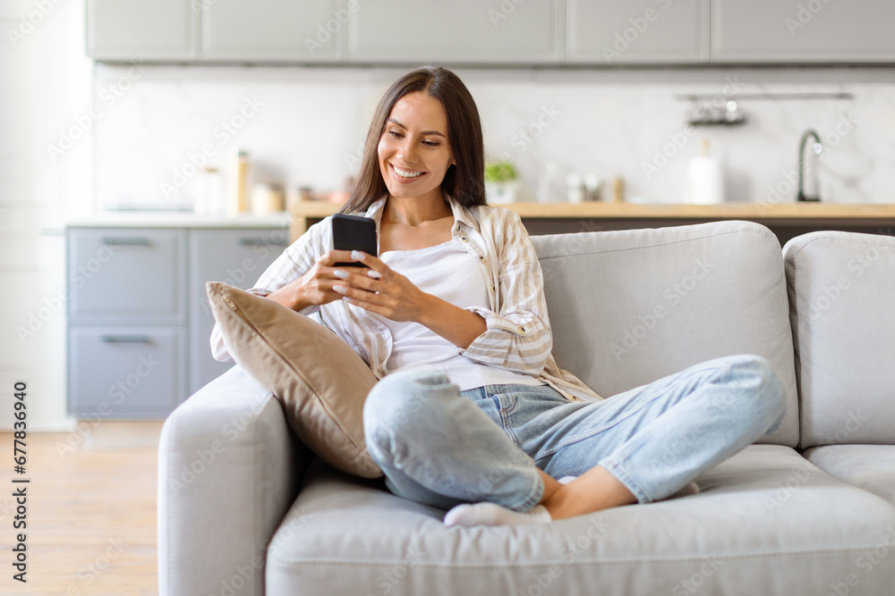 Happy Young Woman Messaging On Smartphone While Relaxing On Couch At Home