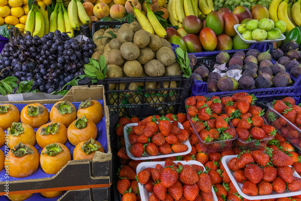 Fruit stand, kiwi, pomegranate, grapes, bananas, strawberries, persimmons.