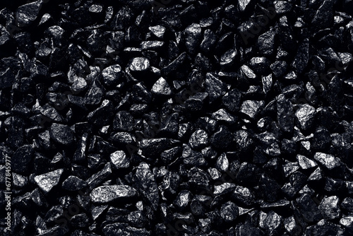 Black background. Black pebbles of irregular shape, evenly poured onto the surface. Monochrome photo.