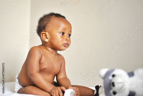 Childcare Concept. Portrait of cute little African  baby wearing bodysuit lying on white bedsheets at home. Black infant child crawling on bed in the bedroom. Selective focus, free copy space photo