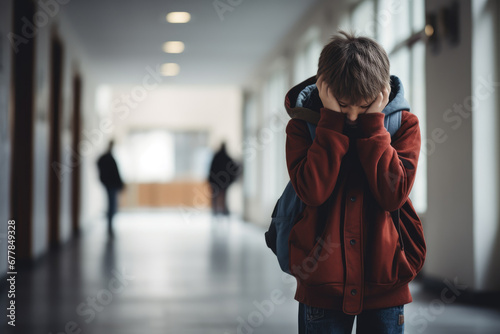 Upset boy covered his face with hands standing alone in school corridor. Learning difficulties, emotions, bullying in school photo