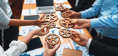 Group of multiracial business people joining gear wheels together over table as effective unity and productive teamwork concept. Efficient system business team process for solution solving. Meticulous