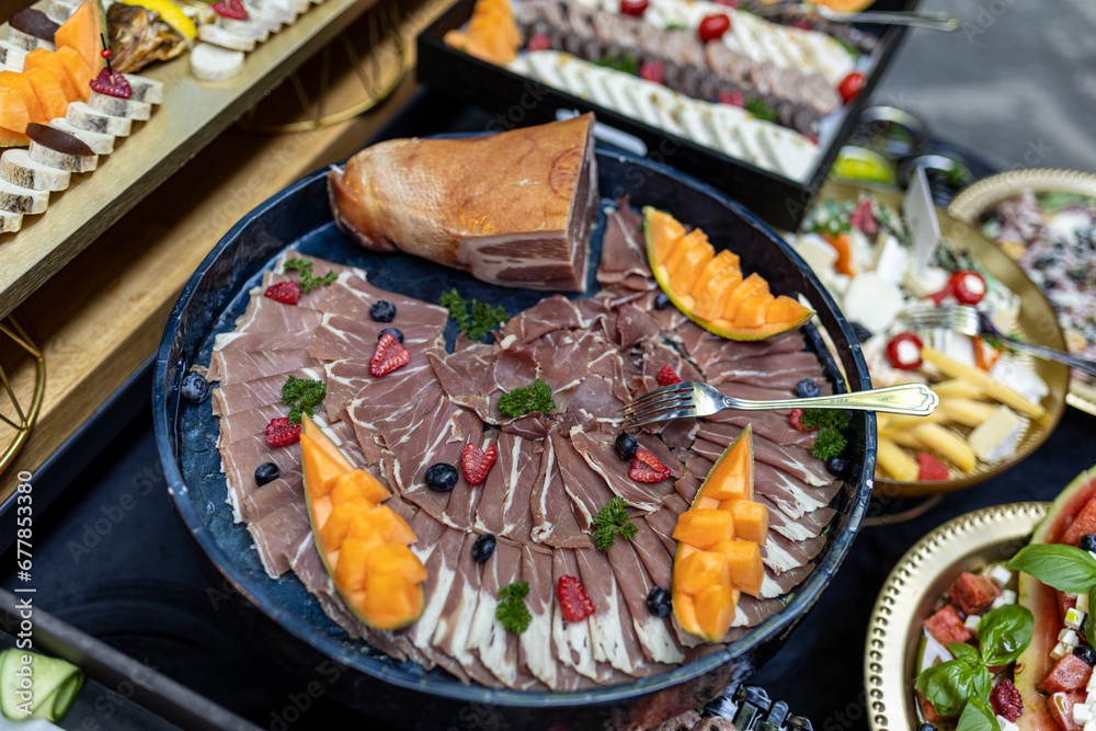 Fototapeta premium Cold meat delicatessen snacks, Italian prosciutto on round black dish on table of restaurant. 