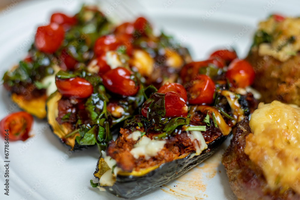 Image focuses on grilled eggplant stuffed with cherry tomatoes, herbs, cheese laid out on platter. 