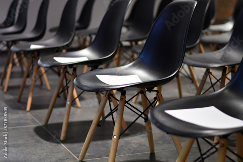 Rows of empty black chairs with white papers in the conference hall. Selective focus. Low DOF