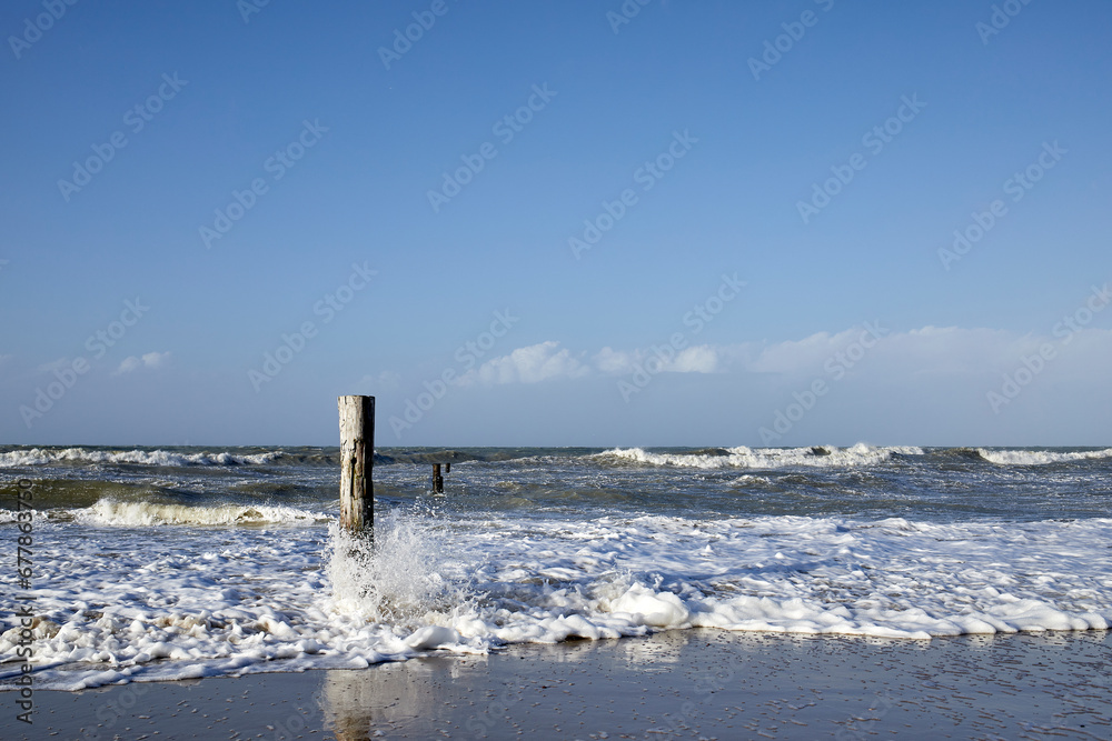 Waves of the North Sea on the beach around a wooden pole