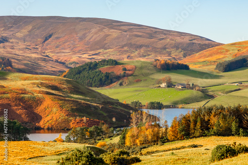 Expansive views of a valley in Scottish Highlands in colourful autumn colours with a lake and a small farm with sheep on a sunny day