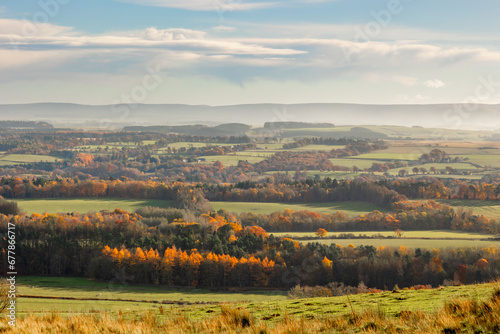 Rolling hills of the Scottish Highlands in colourful autumn with trail and view to fields and towns in light fog. Colourful vibrant trees and woodland