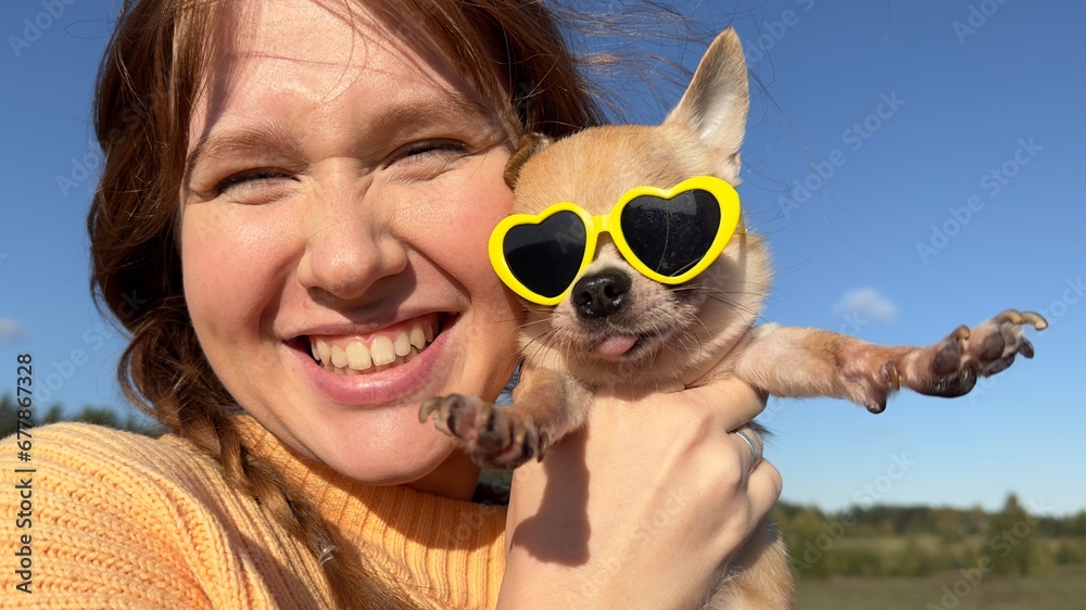 Happy young woman or teenager girl walking with her puppy Chihuahua dog in funny sunglasses in the forest or park at sunny day - obrazy, fototapety, plakaty 