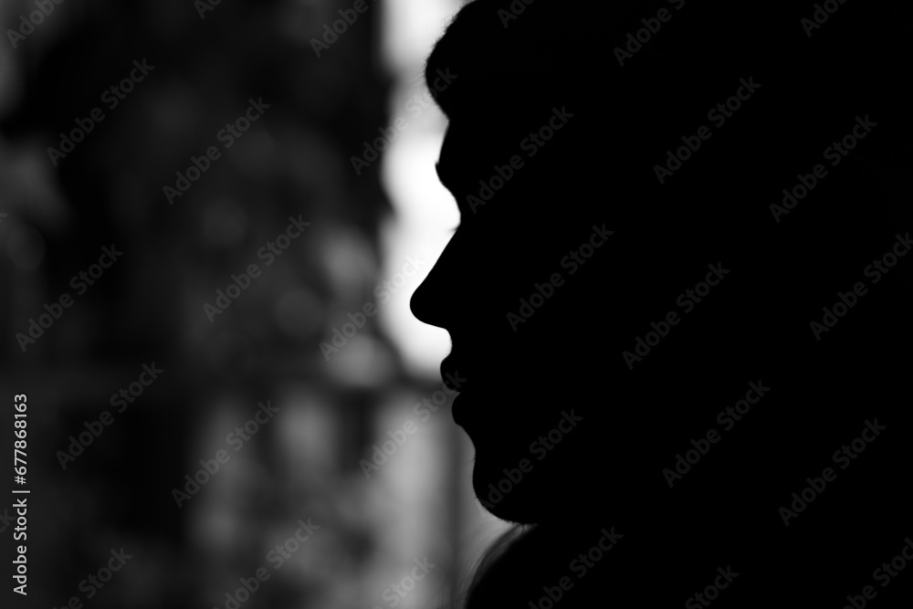 Monochrome silhouette of a young man in profile and backlit by natural light from a window