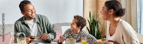 cheerful modern african american family having their breakfast and smiling at each other, banner