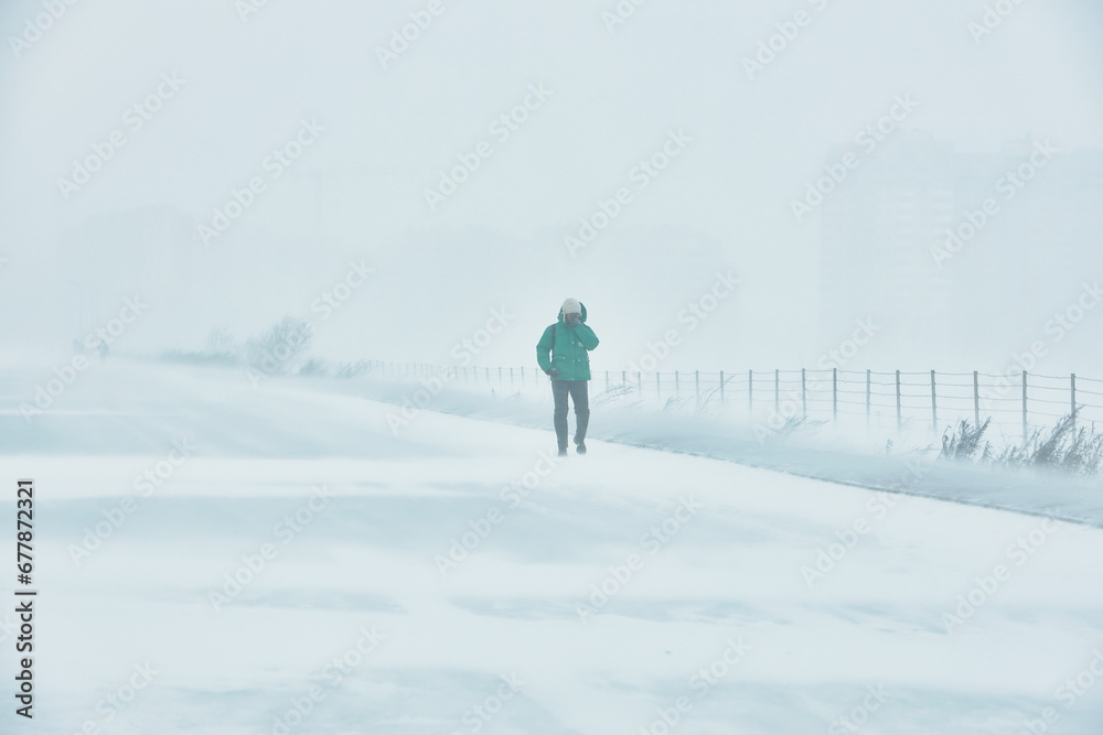A snowstorm. People walk down the street during a snowstorm. Heavy snowfall.  against the background of a cold urban landscape.
