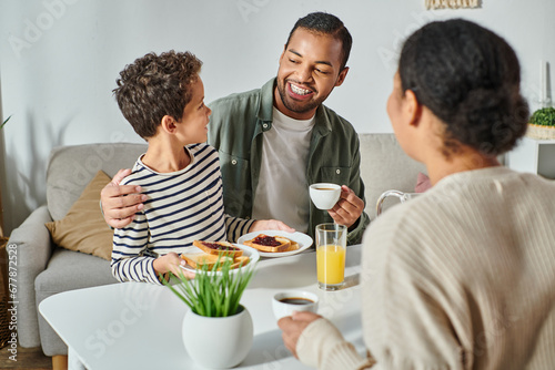 focus on african american father and son smiling at each other with blurred woman looking at them