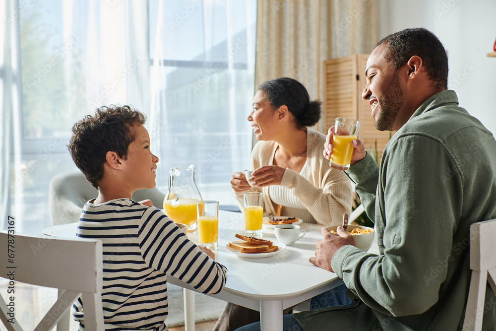 joyful adorable african american boy smiling at his father while his mother looking away, breakfast joyful adorable african american boy smiling at his father while his mother looking away, breakfast