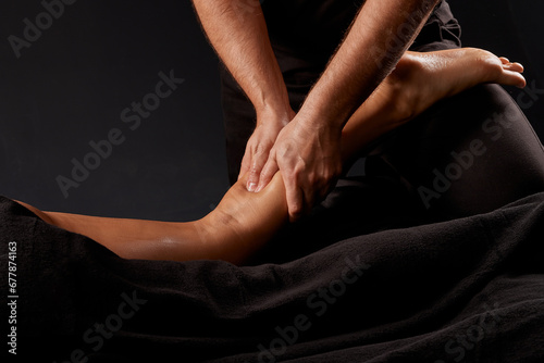 handsome male masseur doing a massage on a girl s leg on a black background  concept of therapeutic relaxing massage