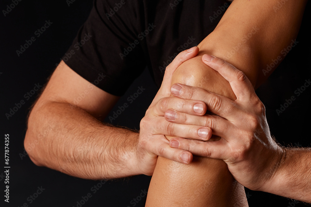 Fototapeta premium A masseur gives a knee massage to a girl on a dark background, massage of the knee joint