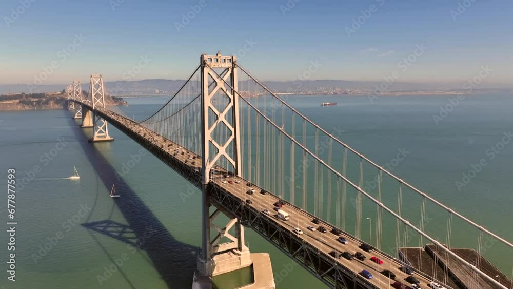 flight along San Francisco–Oakland Bay Bridge, a double-decked suspension spans - across San Francisco Bay - traffic driving on both decks on Interstate 80 - Sailboat crossing below - aerial footage flight along San Francisco–Oakland Bay Bridge, a double-decked suspension spans - across San Francisco Bay - traffic driving on both decks on Interstate 80 - Sailboat crossing below - aerial footage