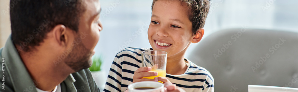 jolly cute african american boy with orange juice smiling at his father with coffee, banner jolly cute african american boy with orange juice smiling at his father with coffee, banner