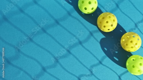 overhead image of yellow and green pickleball balls rolling down a blue court with the shadow of a net cast on the ground