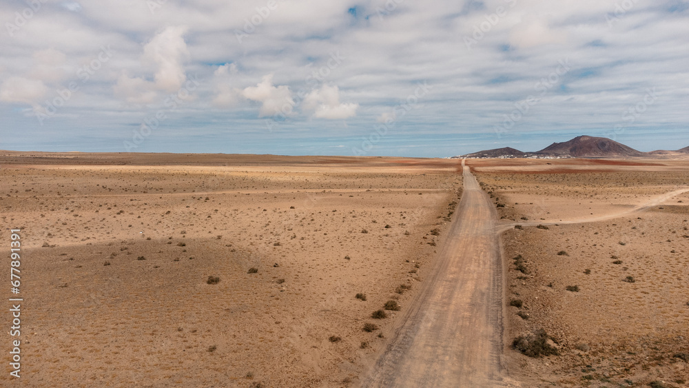 Aereial drone view from above of a convertible car Driving on a rural dirt road in lanzarote, Canary Islands. Desert with clouds car flowers. 