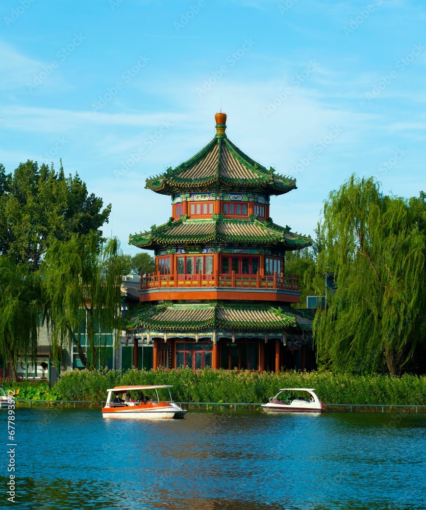 Vertical shot of the Asian pavilion near a lake with people riding electric pedal boats