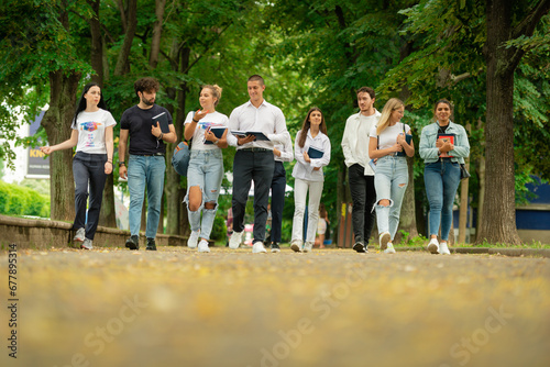 Big young group of college campus students walking together outside with books and backpacks talking to each other going back to school