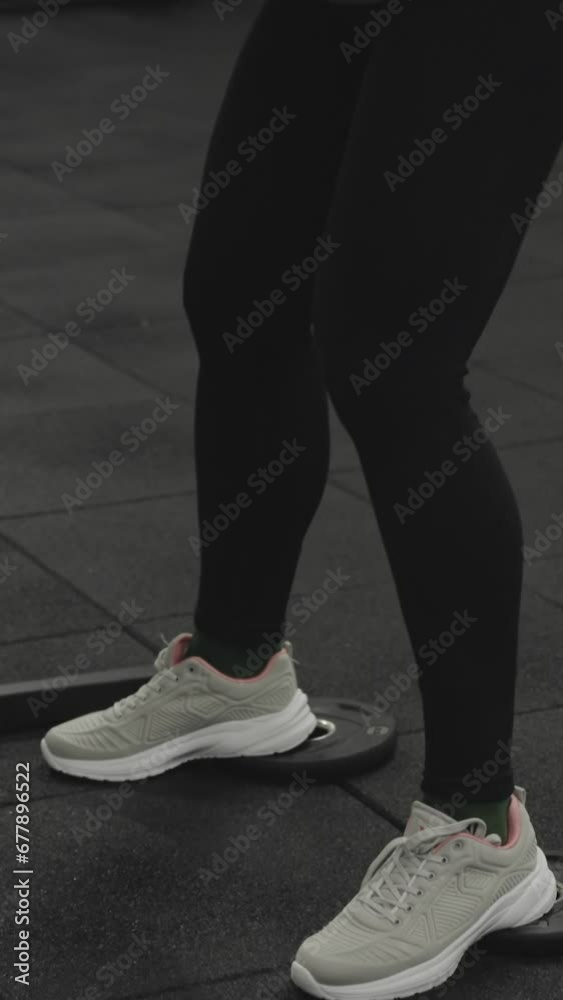 Vertical video. Young athletic woman performing squats with a heavy barbell on her shoulders, using small weight plates under her feet for support. Vertical video. Young athletic woman performing squats with a heavy barbell on her shoulders, using small weight plates under her feet for support.