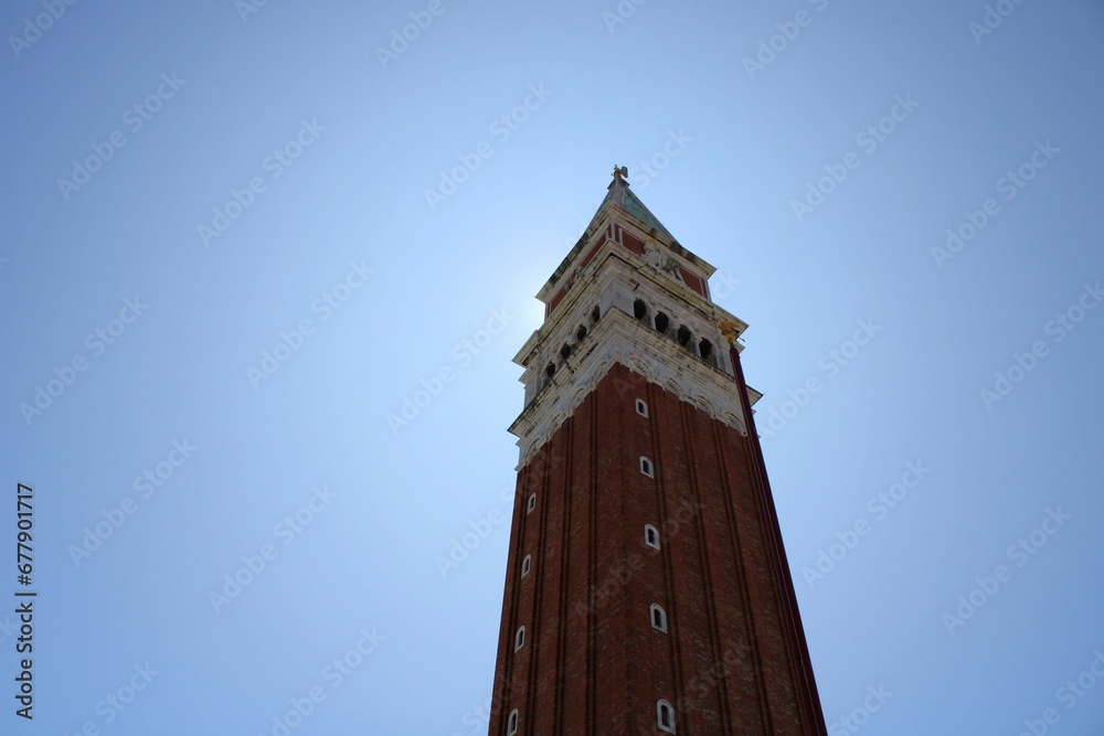 Tall tower of St Mark's Campanile with a clock at the top of it against the blue sky