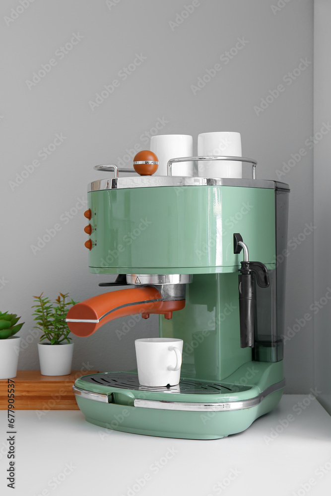 Modern coffee machine with cups on table near white wall Modern coffee machine with cups on table near white wall
