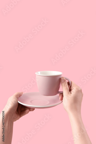 Female hands holding cup and saucer on pink background