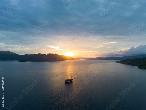 A serene sunrise illuminates the calm seas of Raja Ampat, Indonesia. This remote, equatorial region is known for its high marine biodiversity and is a popular destination for diving and snorkeling.