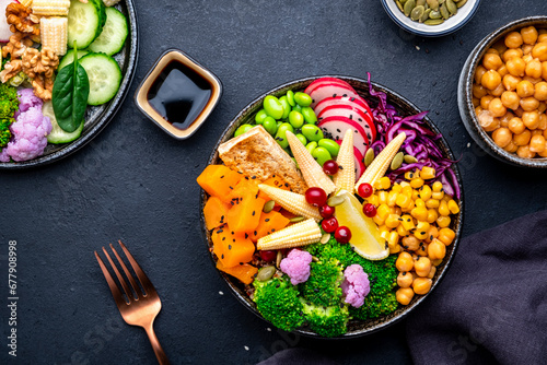 Vegan buddha bowl with sweet potato, quinoa, chickpeas, soybeans edamame, tofu, corn, cabbage, radish, broccoli and seeds, black table background, top view. Autumn or winter healthy vegetarian food