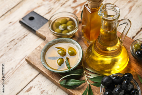 Different glassware and bowls with fresh olive oil on white wooden background