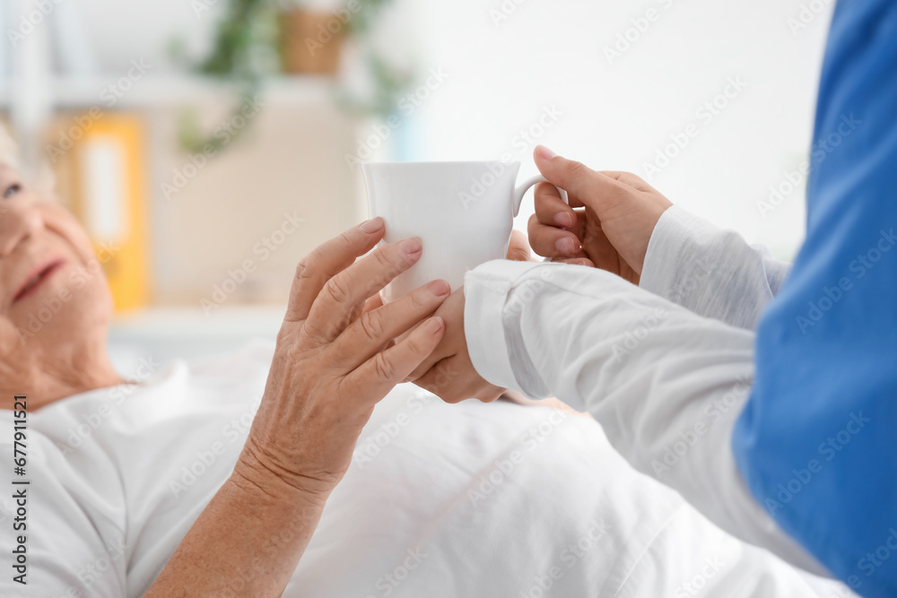 Senior woman taking cup of tea from nurse in bedroom Senior woman taking cup of tea from nurse in bedroom