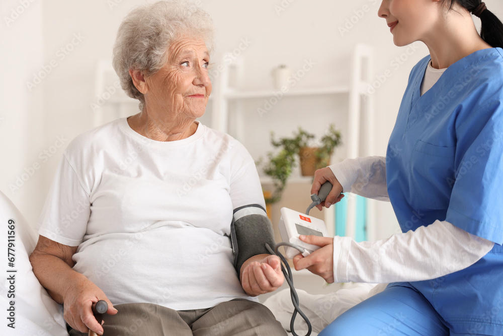 Obraz premium Female nurse measuring blood pressure of senior woman in bedroom