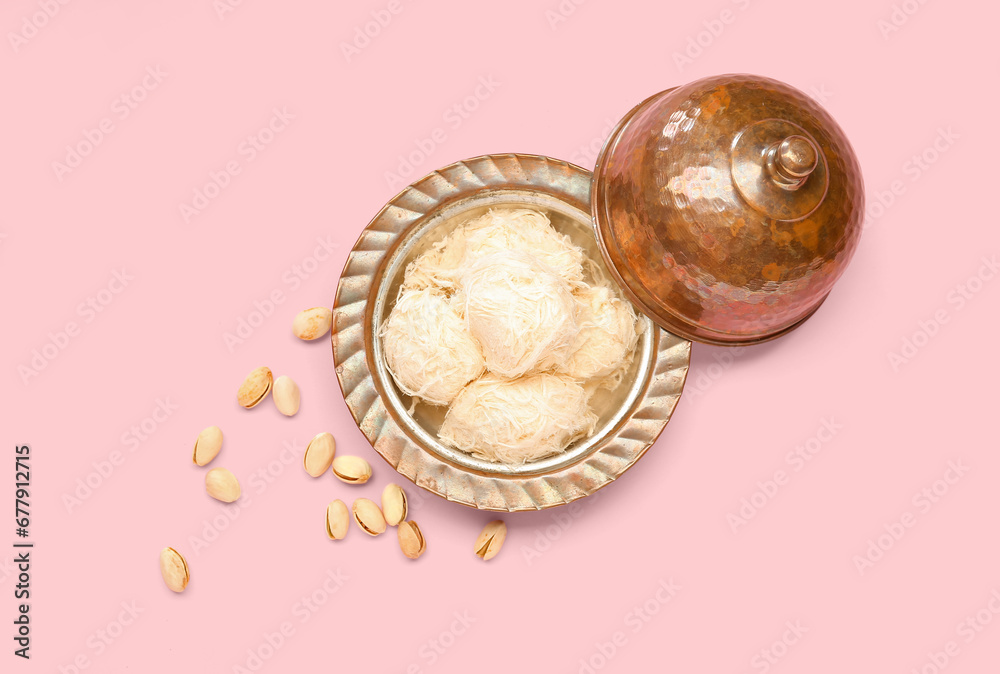 Bowl with tasty Turkish Pismaniye and pistachios on pink background