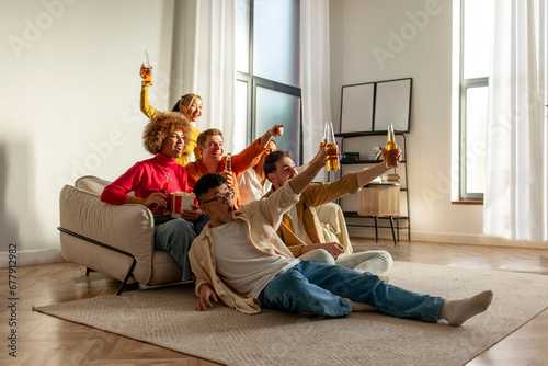multiracial group of young friends sitting on the couch at home drinking beer and watching TV and celebrating good luck photo