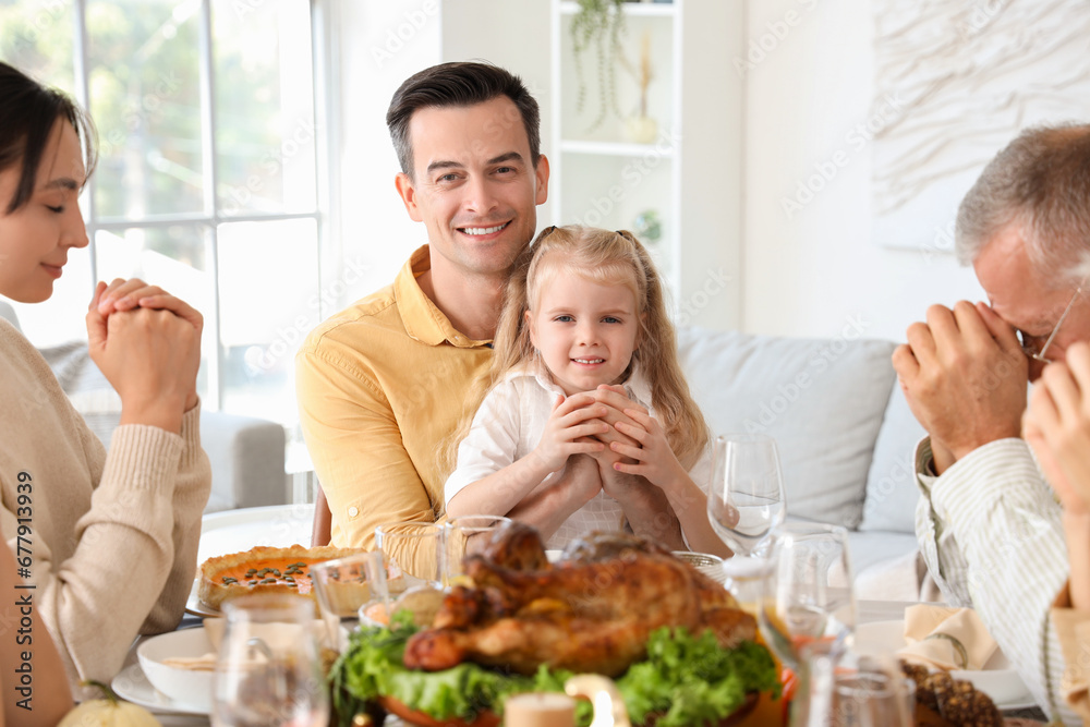 Happy family praying before dinner at festive table on Thanksgiving Day Happy family praying before dinner at festive table on Thanksgiving Day