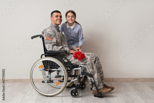 Soldier in wheelchair with flowers and his little daughter on light background. Veterans Day celebration