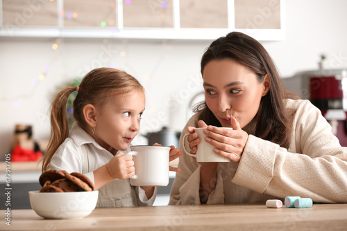 Young mother with her little daughter drinking hot chocolate at home on Christmas eve