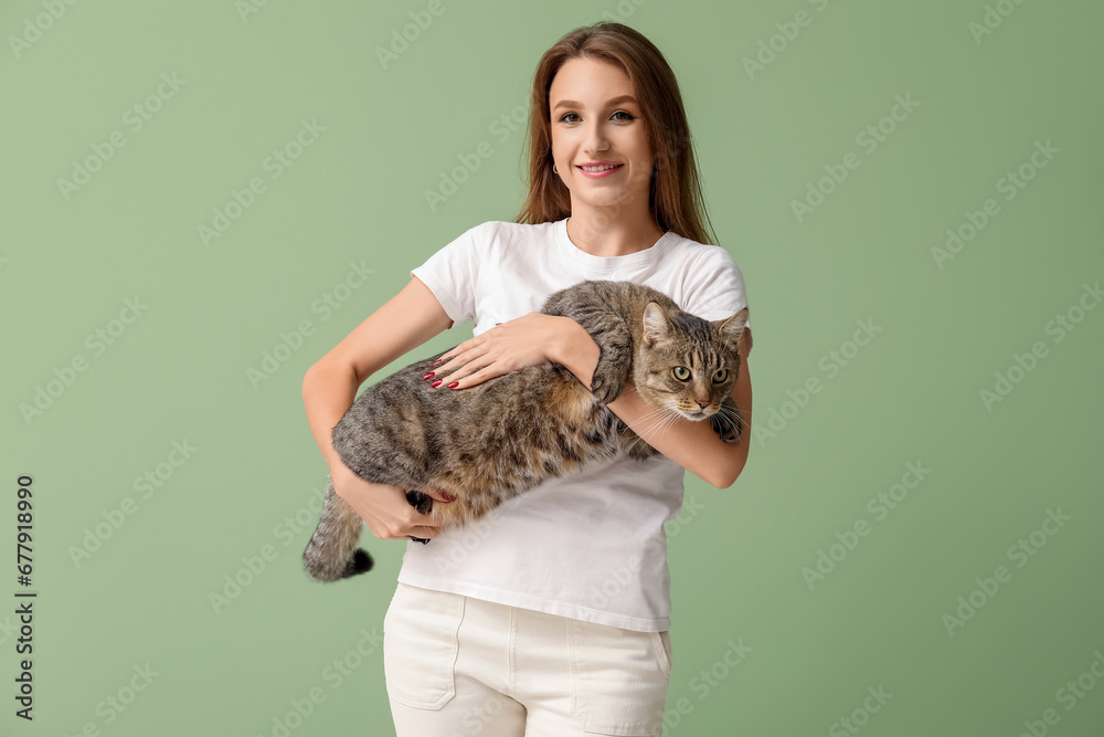 Pretty young woman with cute tabby cat on green background
