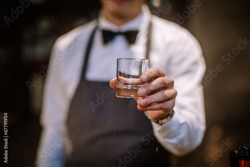 hands of a male bartender accurate holding clean transparent empty glass for booze. Blurred bar background