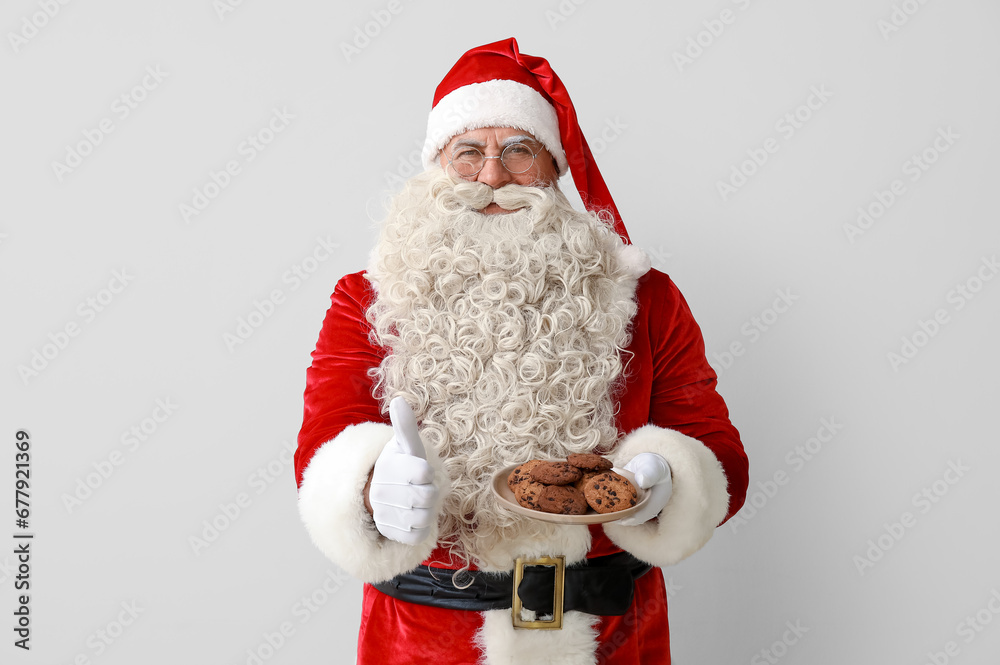 Santa Claus with plate of tasty cookies showing thumb-up on white background Santa Claus with plate of tasty cookies showing thumb-up on white background