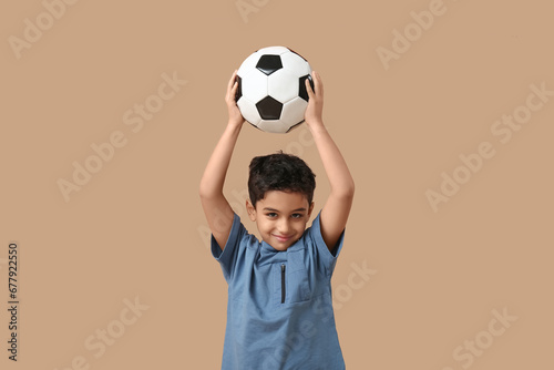 Cute little boy with soccer ball on beige background