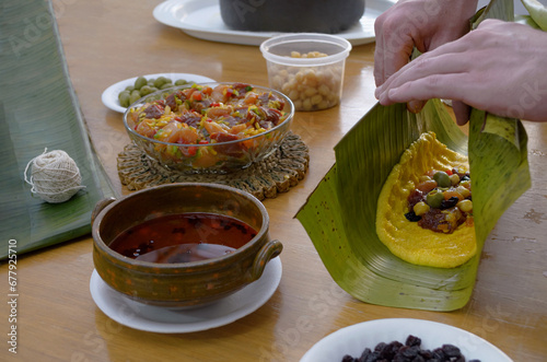 Elaboración de hallacas venezolanas. Plato tradicional navideño con masa de maíz, guiso crudo de carne y pollo, aceitunas, garbanzos, pasas y onoto. Manos envolviendo una hallaca en hojas de plátano. photo